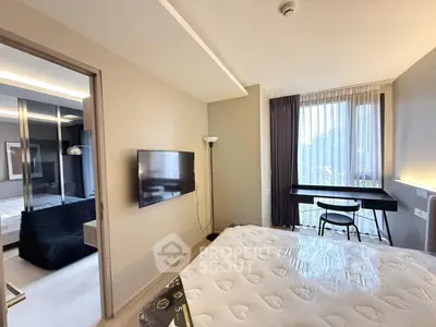 Modern bedroom with natural light, featuring a wall-mounted TV and a sleek workspace by the window.