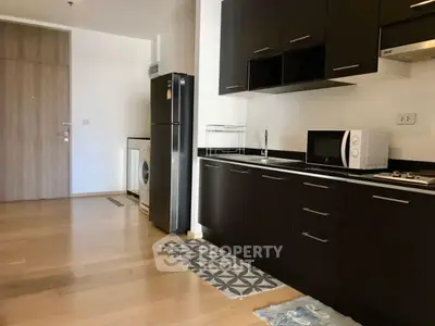 Modern kitchen with dark cabinets, fridge, and washing machine in open layout apartment.
