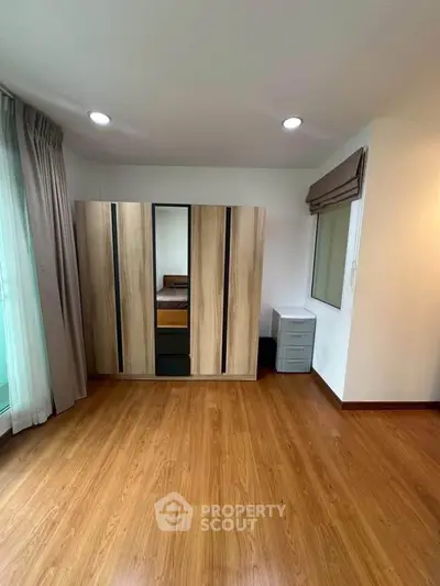 Spacious bedroom with wooden flooring and modern wardrobe in a bright apartment.