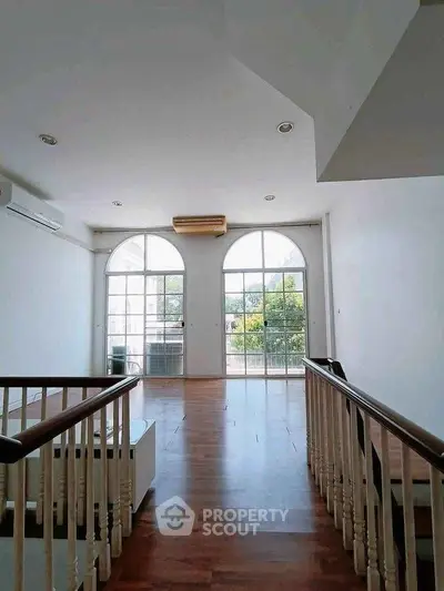 Spacious living room with large windows and wooden flooring, offering abundant natural light.