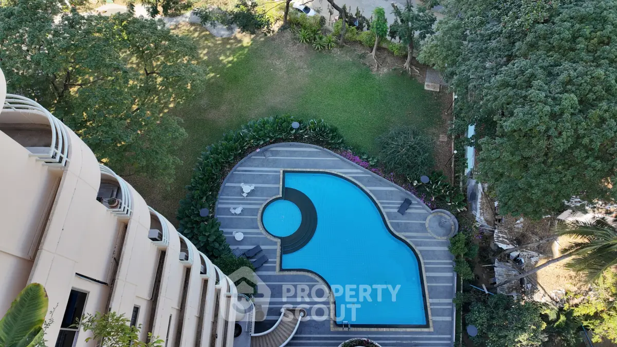 Stunning aerial view of luxury apartment pool surrounded by lush greenery, perfect for relaxation and leisure.
