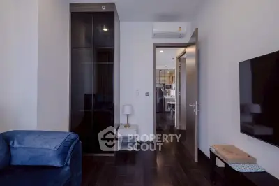 Modern living room with sleek furniture and open view to kitchen area, featuring dark wood flooring and minimalist decor.