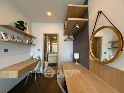 Modern study room with wooden desk, shelves, and stylish decor leading to a bathroom.