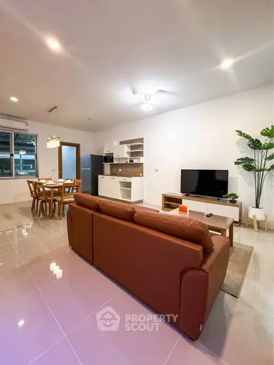 Spacious modern living room with open kitchen and dining area, featuring sleek furniture and bright lighting.