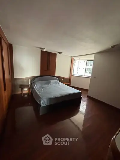 Spacious bedroom with wooden flooring and large window offering natural light.