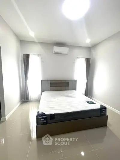 Spacious bedroom with modern design and natural light, featuring a comfortable bed and air conditioning.