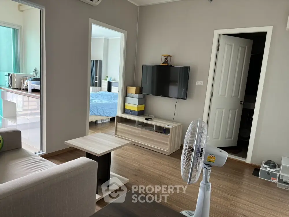 Modern living room with wooden flooring, wall-mounted TV, and open view to bedroom