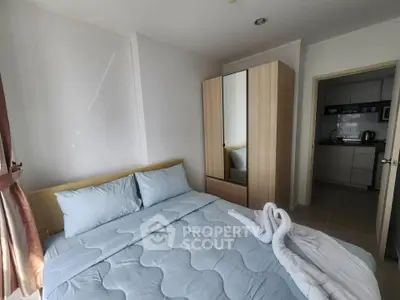 Cozy bedroom with soft blue bedding and mirrored wardrobe, adjacent to a compact kitchen area.