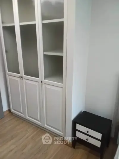 Spacious bedroom with elegant white wardrobe and stylish nightstand on wooden flooring.