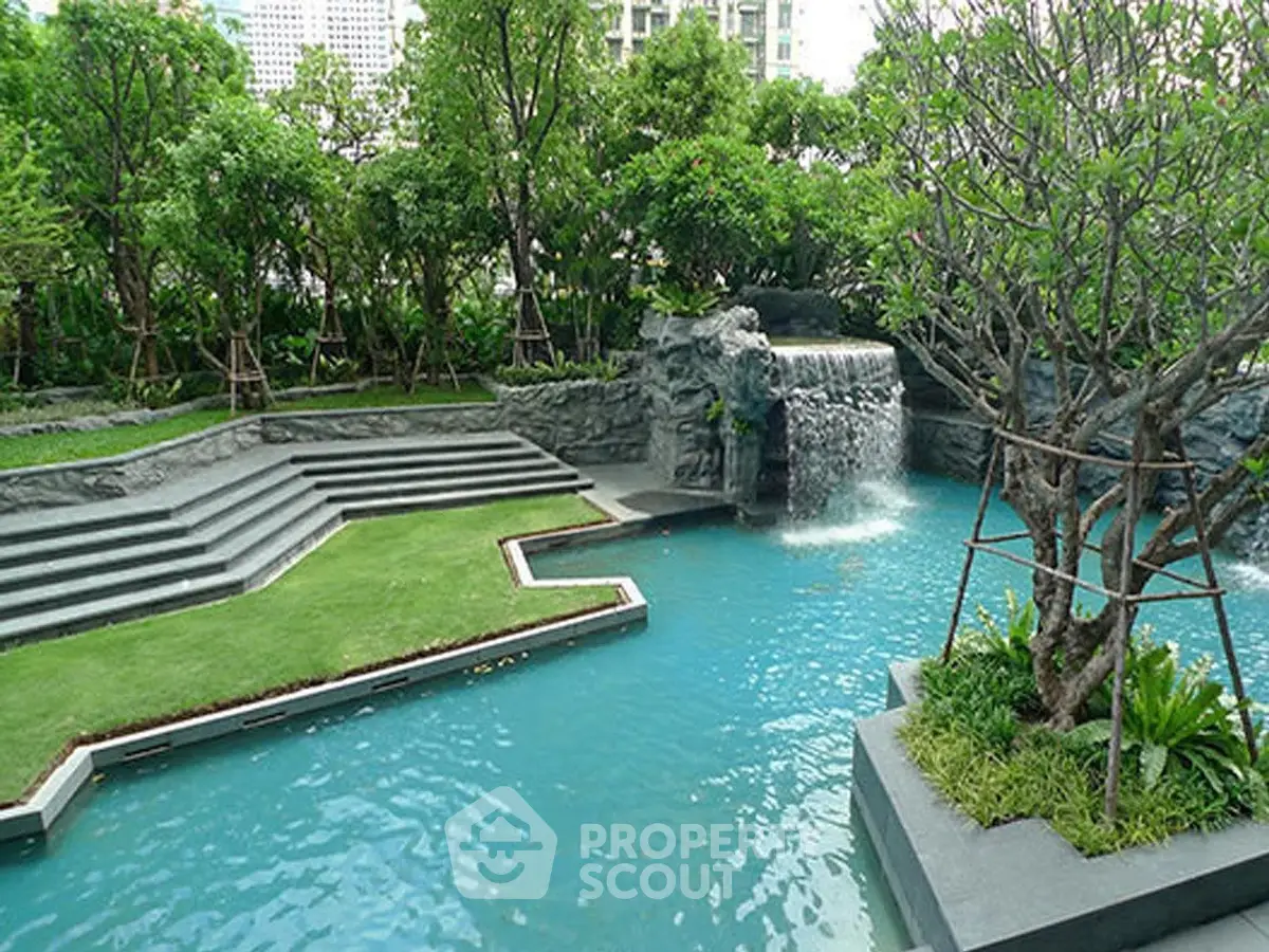 Luxurious outdoor pool with waterfall feature and lush greenery in a modern residential complex.