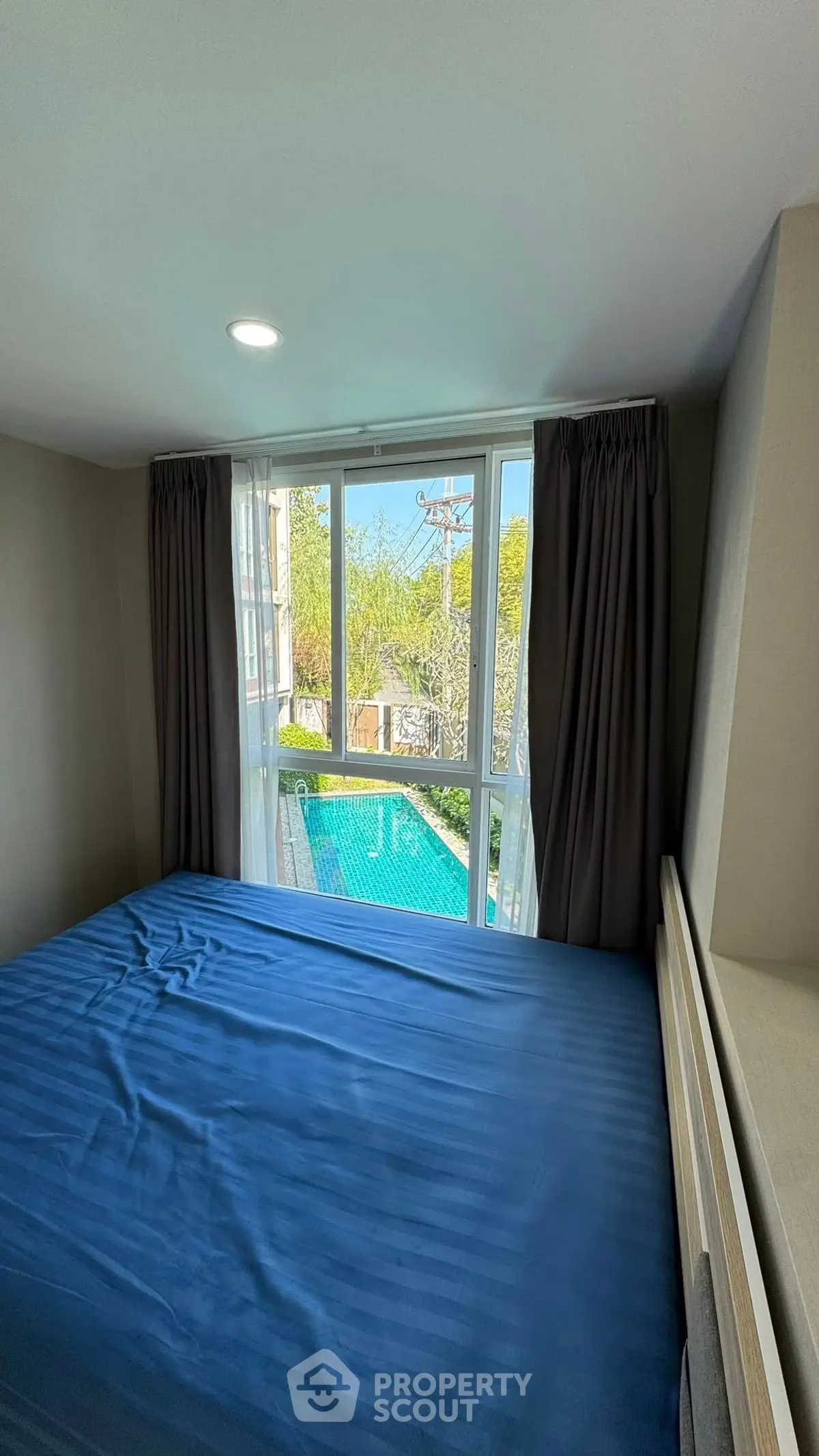 Cozy bedroom with pool view, featuring large window and blue bedding for a serene atmosphere.