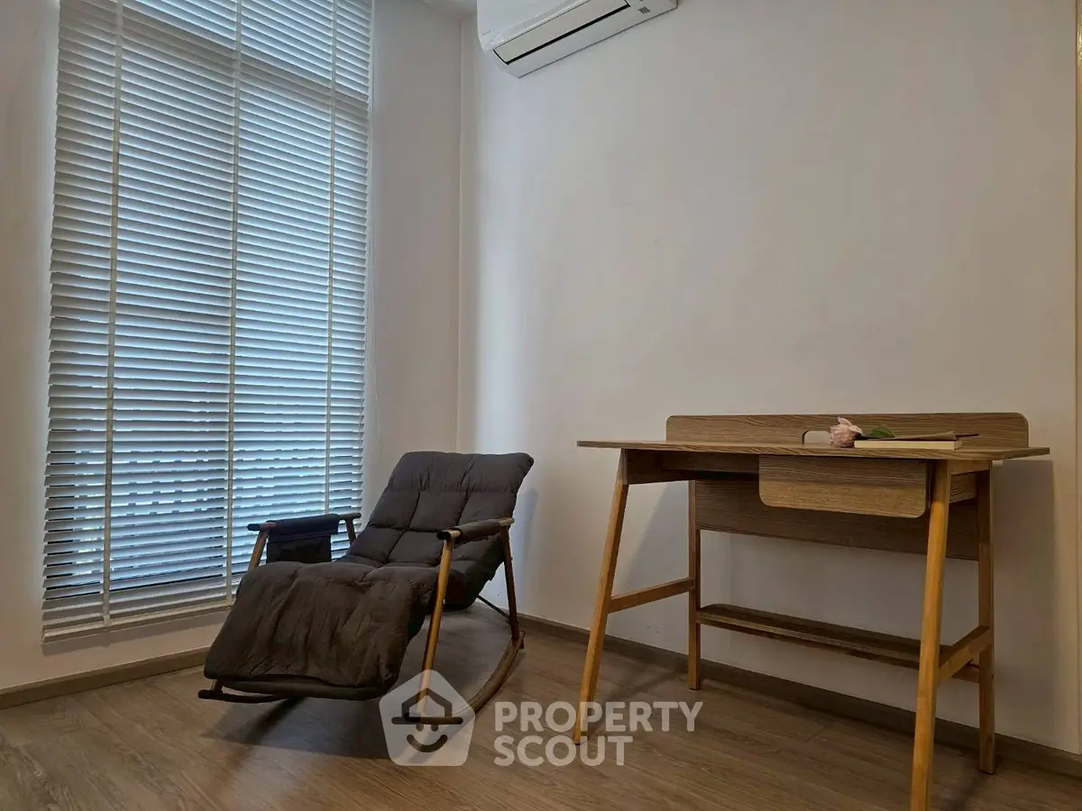 Minimalist study room with rocking chair and wooden desk, featuring floor-to-ceiling window blinds.