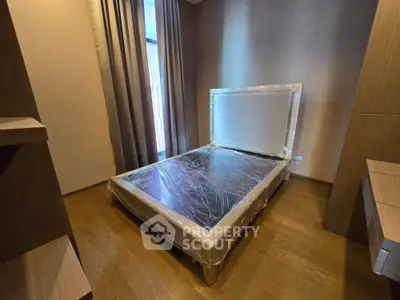 Modern bedroom with new bed wrapped in protective plastic, showcasing sleek wooden flooring and elegant curtains.