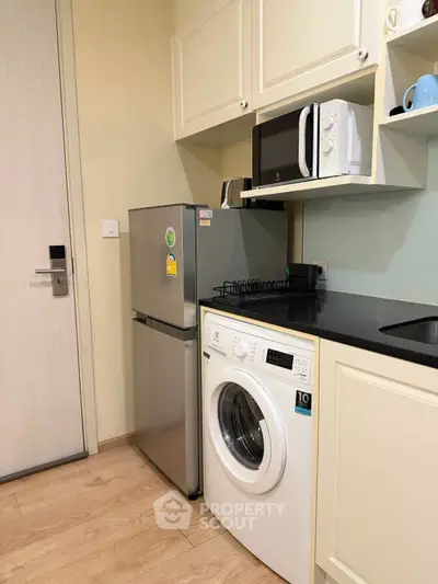 Modern kitchen with washing machine, fridge, and microwave in compact layout.
