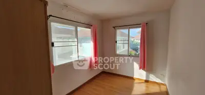 Bright bedroom with wooden floor and large windows, featuring pink curtains and natural light.