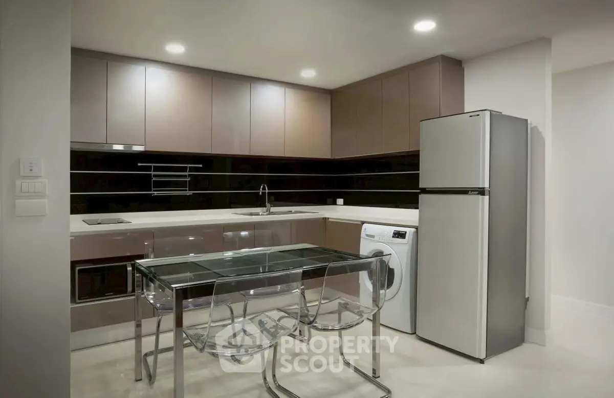 Modern kitchen with sleek cabinets, glass dining table, and stainless steel appliances.