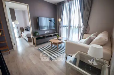 Modern living room with sleek furniture and large TV, adjacent to a cozy bedroom.