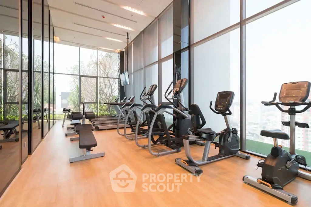 Modern gym with state-of-the-art equipment and floor-to-ceiling windows in luxury building.