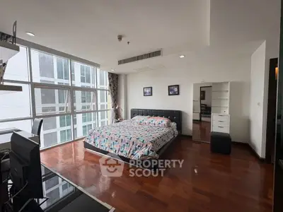 Spacious bedroom with large windows and modern furnishings in a high-rise apartment.