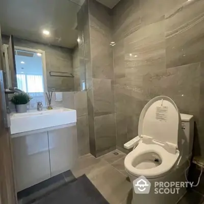 Modern bathroom with sleek gray tiles, white fixtures, and a well-lit mirror creating a serene and clean atmosphere.