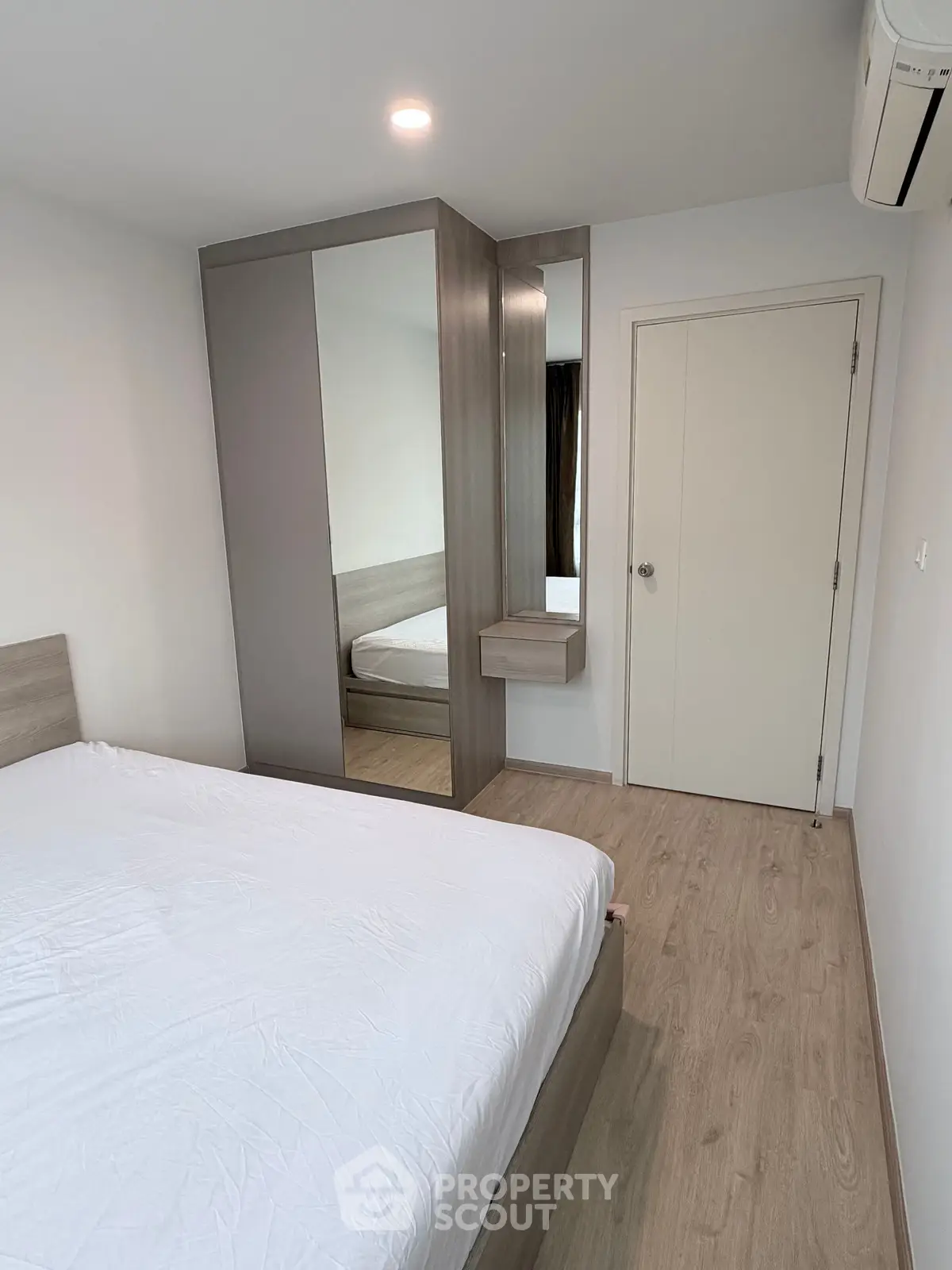 Modern bedroom with wooden flooring, mirrored wardrobe, and air conditioning unit.