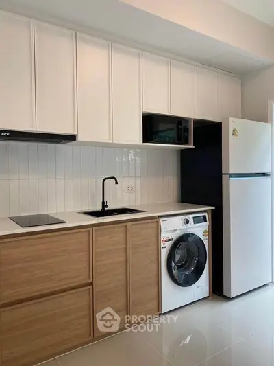 Modern kitchen with sleek cabinets, washing machine, and fridge in a stylish apartment.