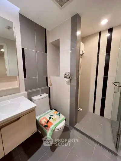 Modern bathroom with sleek tiles and glass shower enclosure in contemporary apartment.