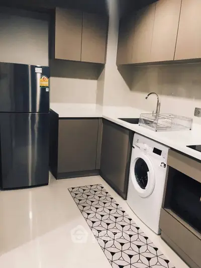 Modern kitchen with sleek cabinets, washing machine, and stainless steel fridge in a compact layout.
