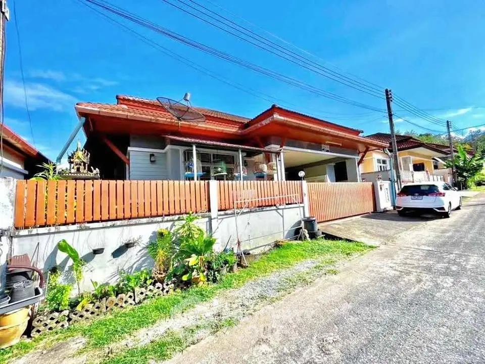 Charming suburban house with red roof and fenced yard under clear blue sky.