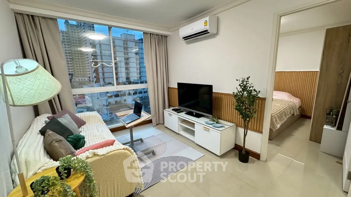 Modern living room with cozy decor and city view, adjacent to a stylish bedroom.
