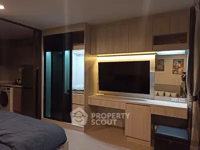 Modern studio apartment with sleek wooden cabinetry and built-in TV, featuring a cozy bed and compact kitchen area.