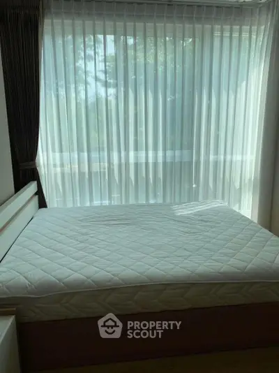 Bright bedroom with large window and sheer curtains, featuring a comfortable bed.