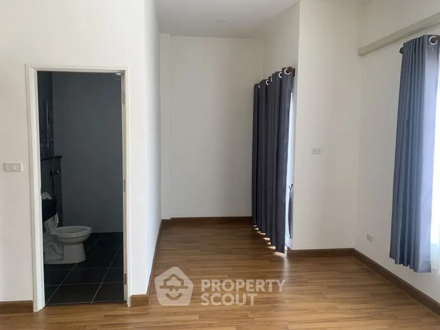 Spacious room with wooden flooring and attached bathroom, ideal for modern living.