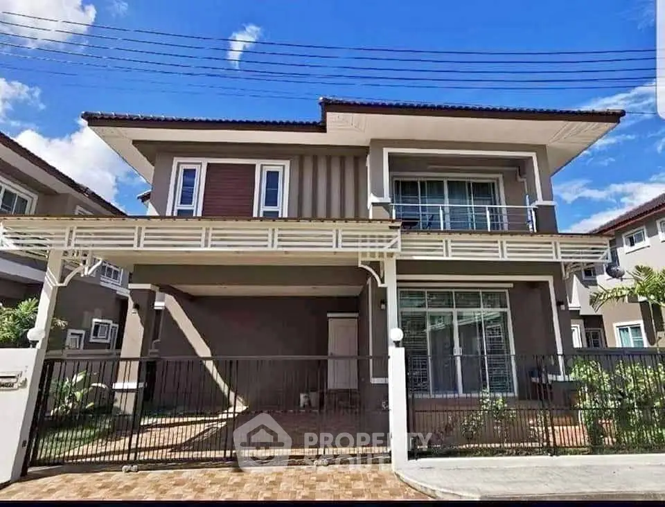 Stunning two-story modern house with spacious balcony and gated driveway under clear blue skies.