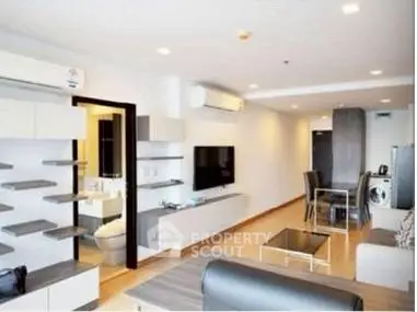 Modern living room with sleek furniture and open layout, featuring a wall-mounted TV and dining area.