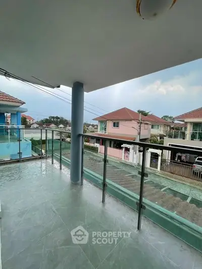 Spacious balcony with glass railing offering a serene neighborhood view in a modern residential area.