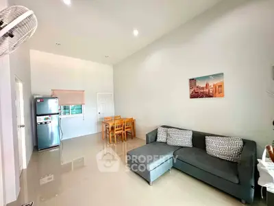 Modern living room with sleek furniture and dining area, featuring a stylish gray sofa and stainless steel fridge.