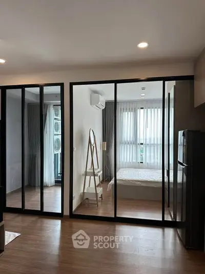 Modern apartment with glass partition, cozy bedroom, and sleek wooden flooring.