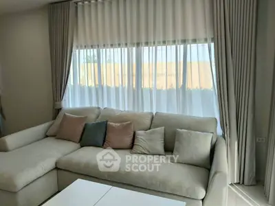Elegant living room with plush sofa and large window draped in sheer curtains, offering a cozy and inviting atmosphere.