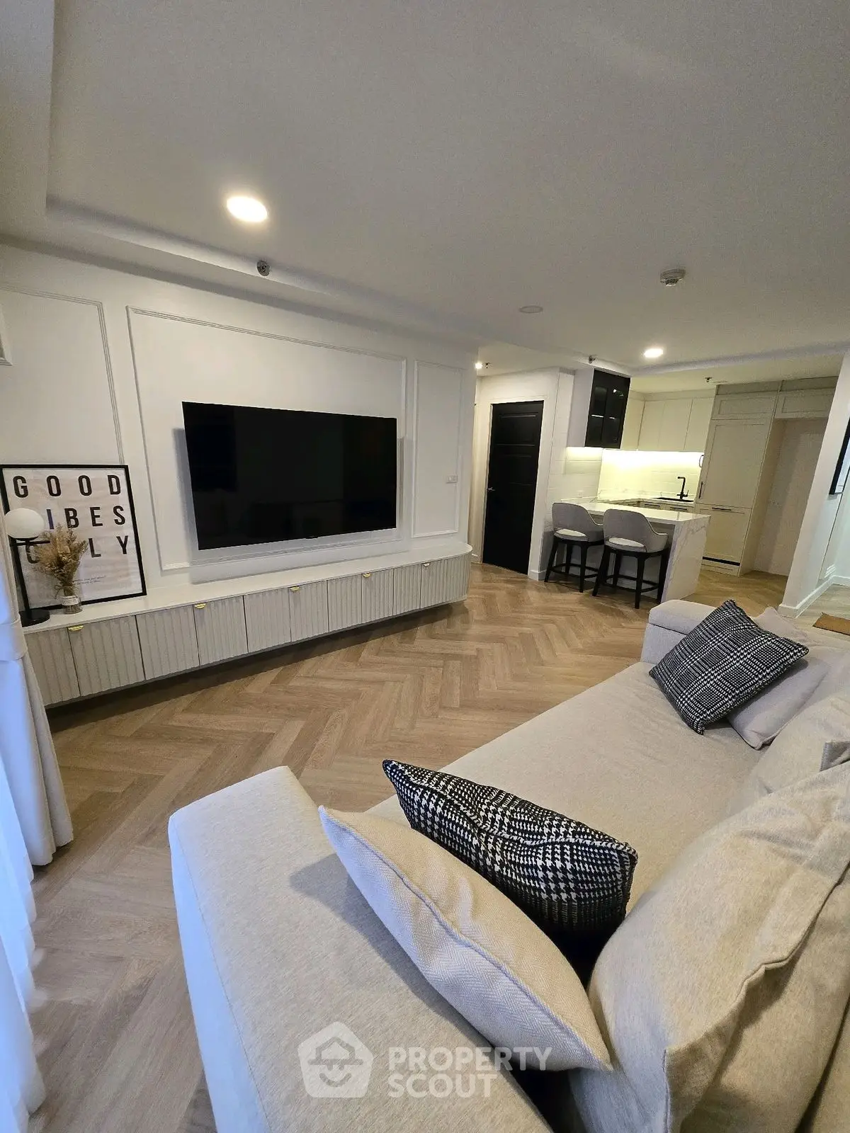Modern living room with stylish decor and open kitchen layout, featuring a large TV and cozy seating area.