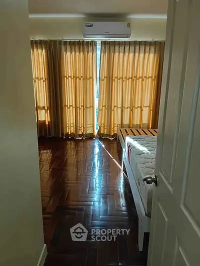 Spacious bedroom with wooden flooring and large windows for natural light.