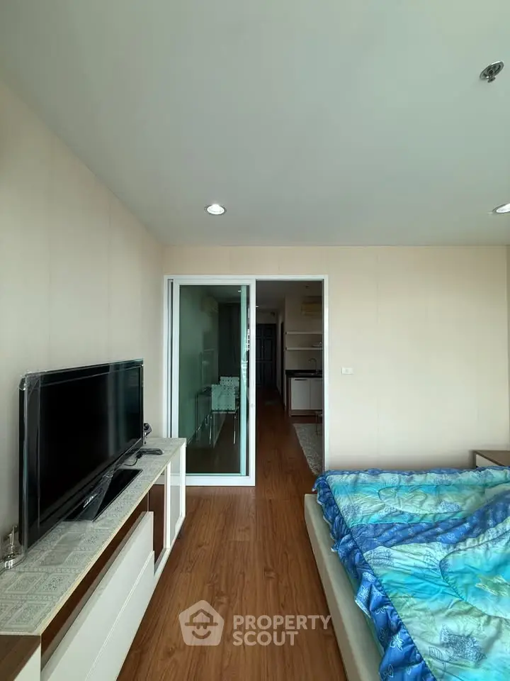 Modern bedroom with wooden flooring and sliding glass doors leading to a hallway, featuring a TV and stylish decor.