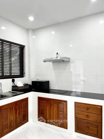 Modern kitchen with sleek white tiles and wooden cabinets, featuring an electric stove and range hood.
