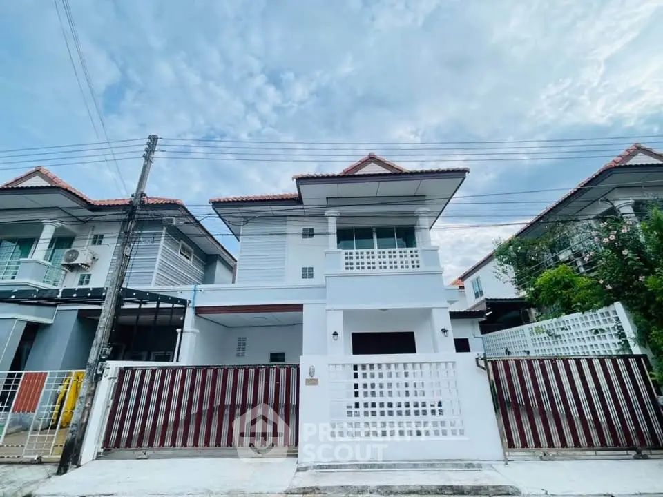Charming two-story white house with red roof tiles and gated entrance in a serene neighborhood.