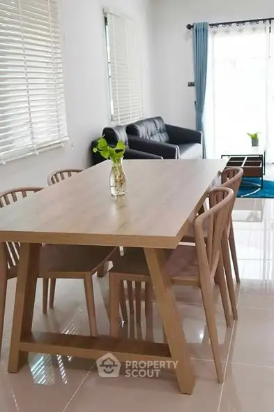 Modern dining area with wooden table and chairs, adjacent to a cozy living room with natural light.