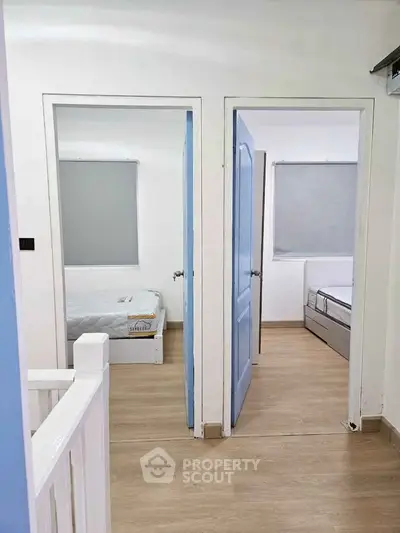 Bright hallway leading to two cozy bedrooms with wooden flooring and minimalist decor.