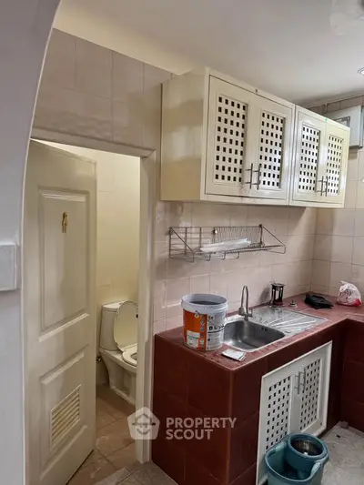 Compact kitchen with adjacent bathroom, featuring tiled countertops and overhead cabinets.