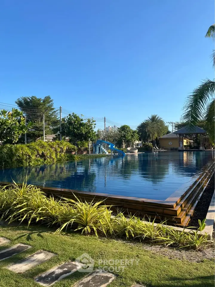 Luxurious outdoor pool with lush greenery and clear blue sky, perfect for relaxation and leisure.