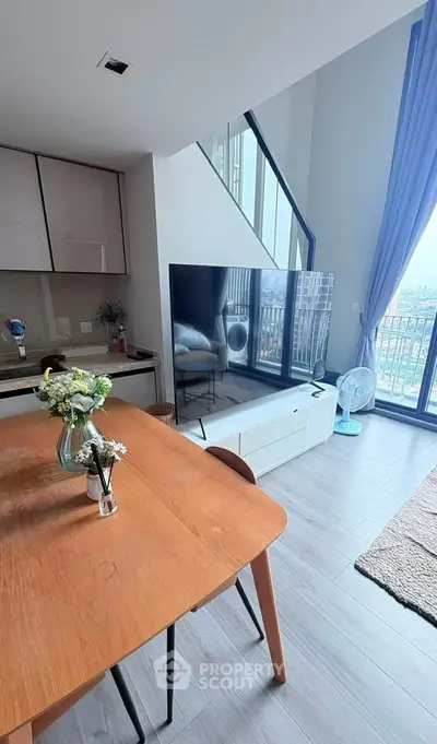 Modern living room with large TV, dining table, and balcony view in a stylish apartment.