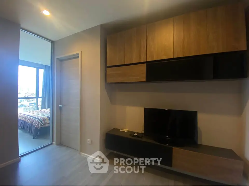 Modern living room with sleek wooden cabinetry and TV, adjacent to a cozy bedroom with city view.